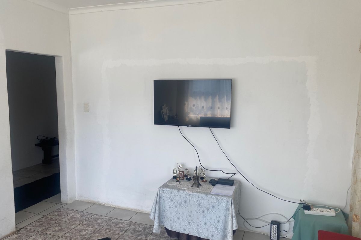 Living room area featuring tiled flooring and a wall-mounted television, requiring minor cosmetic attention to the wall finish.