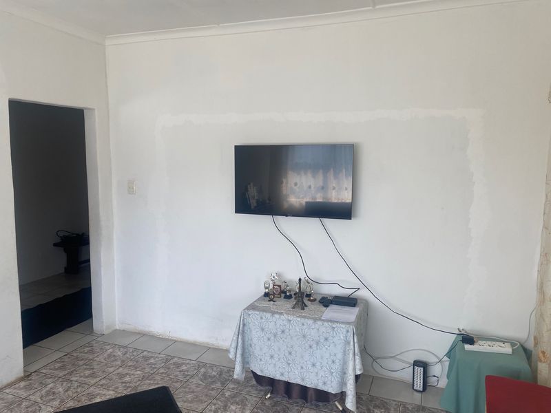 Living room area featuring tiled flooring and a wall-mounted television, requiring minor cosmetic attention to the wall finish.