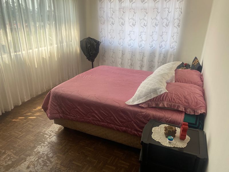 A bedroom featuring parquet flooring and large windows with sheer curtains, offering a bright space with potential for cosmetic updates.