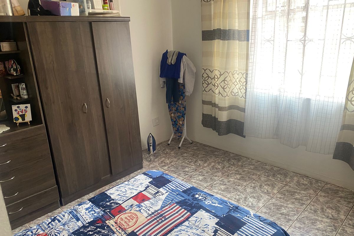 A bedroom featuring tiled flooring and a window fitted with security bars, providing natural light.