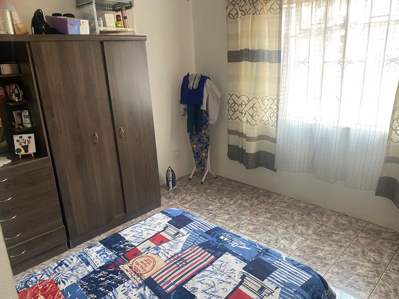 A bedroom featuring tiled flooring and a window fitted with security bars, providing natural light.