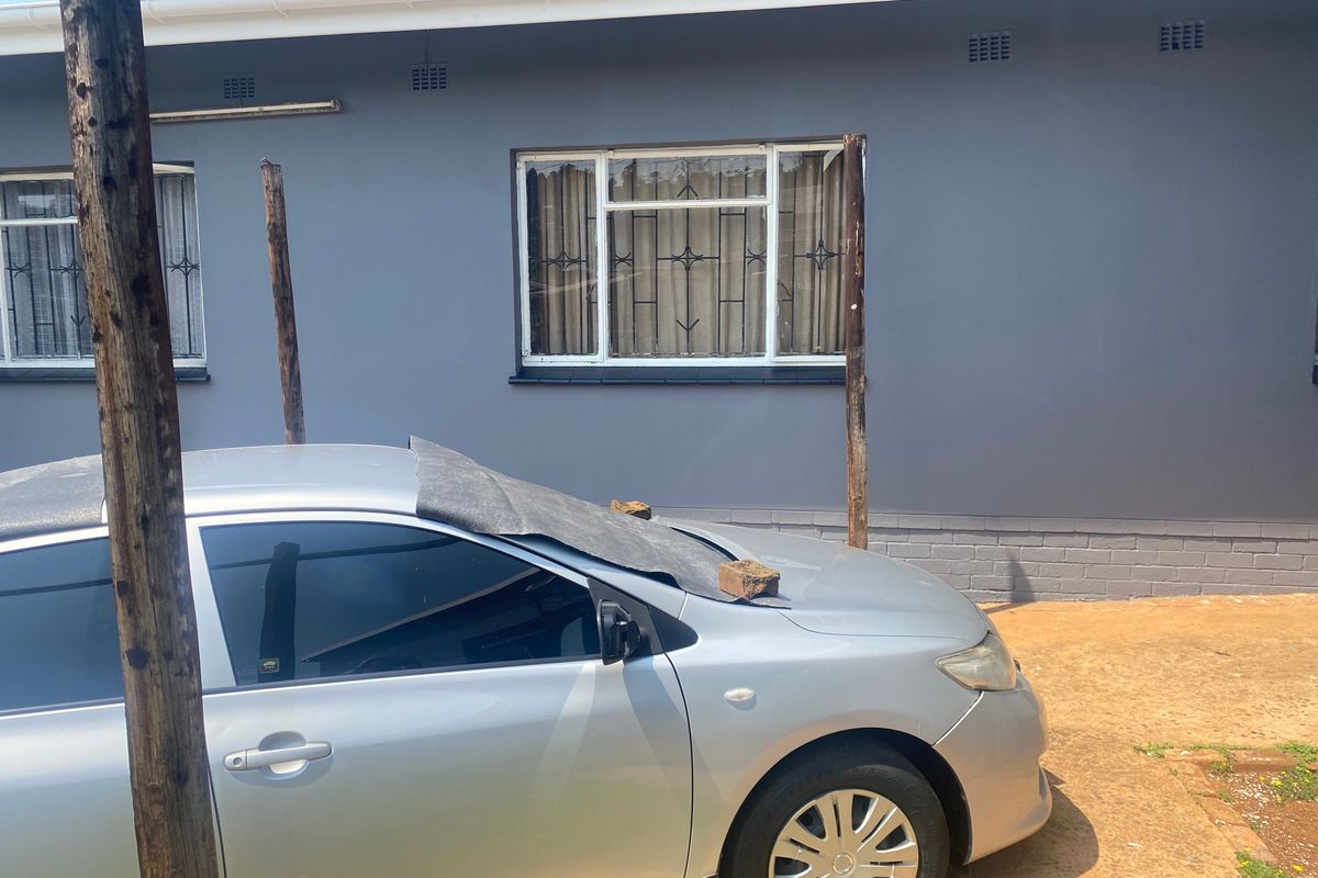 Rear exterior view of the house featuring grey painted walls, white window frames with security bars, and guttering.