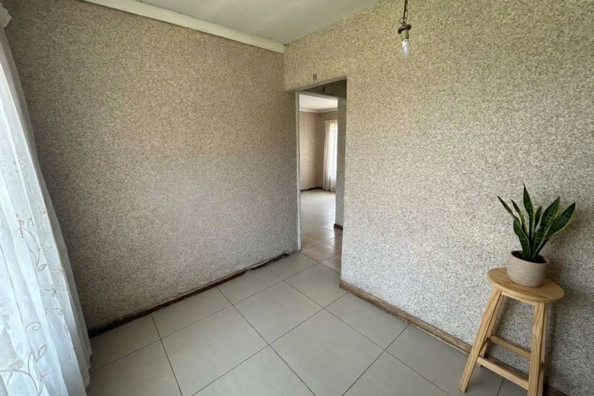 An empty living area featuring neutral tiled flooring and textured wallpaper, offering a blank canvas for renovation and interior design updates.