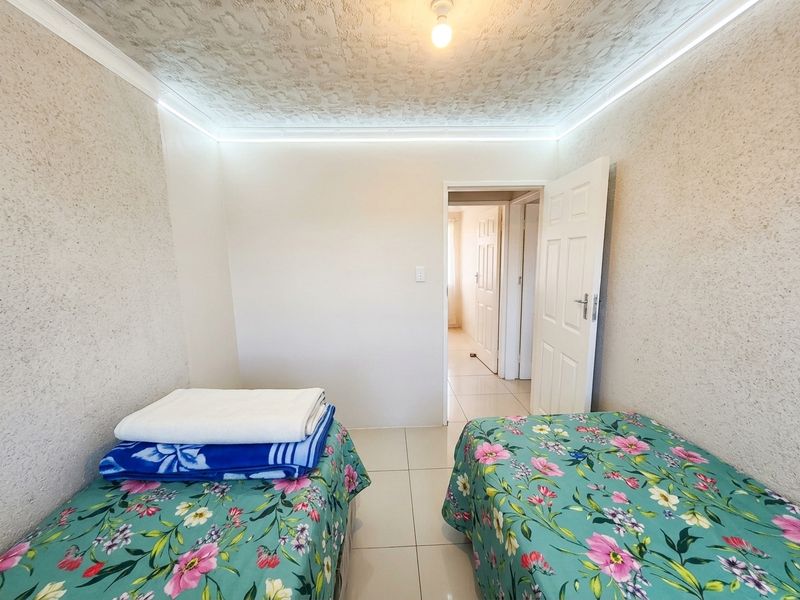 A bedroom featuring tiled flooring, textured ceiling finishes, and integrated cove lighting, providing a functional space with direct access to the hallway.