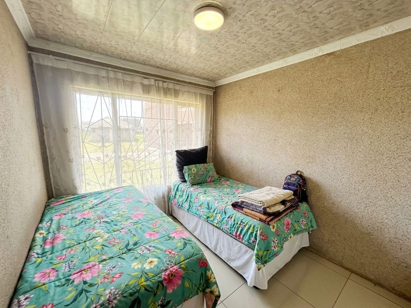 A compact bedroom featuring tiled flooring, textured wall and ceiling finishes, and a window fitted with a security gate.