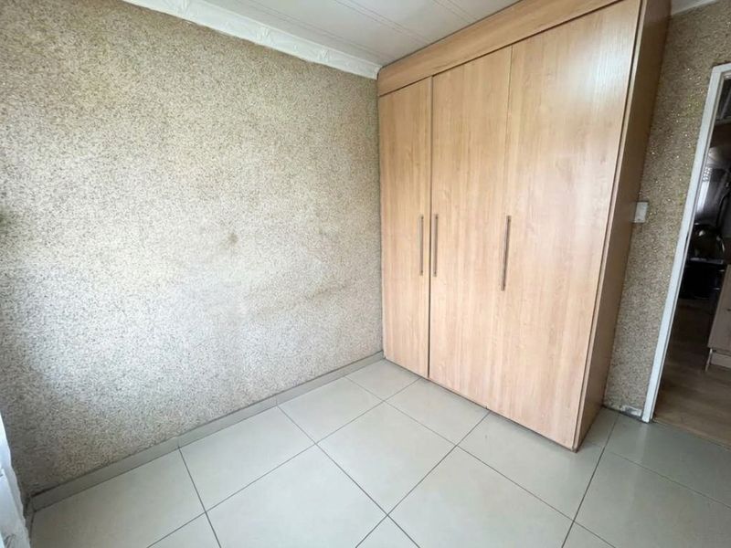 A bedroom featuring tiled flooring, built-in wooden wardrobes, and textured wallpaper in need of cosmetic attention.