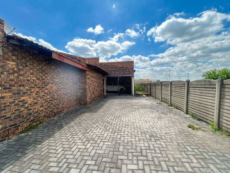 A paved rear driveway area featuring a brick boundary wall, precast concrete fencing, and a secure metal gate leading to a garage.