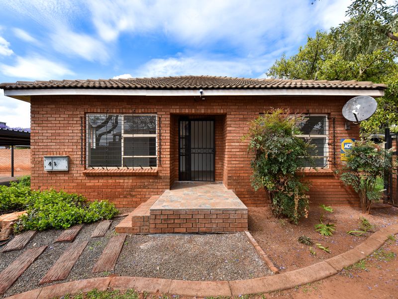 Front elevation of a face brick house featuring a tiled roof, security gate, and security bars on windows.