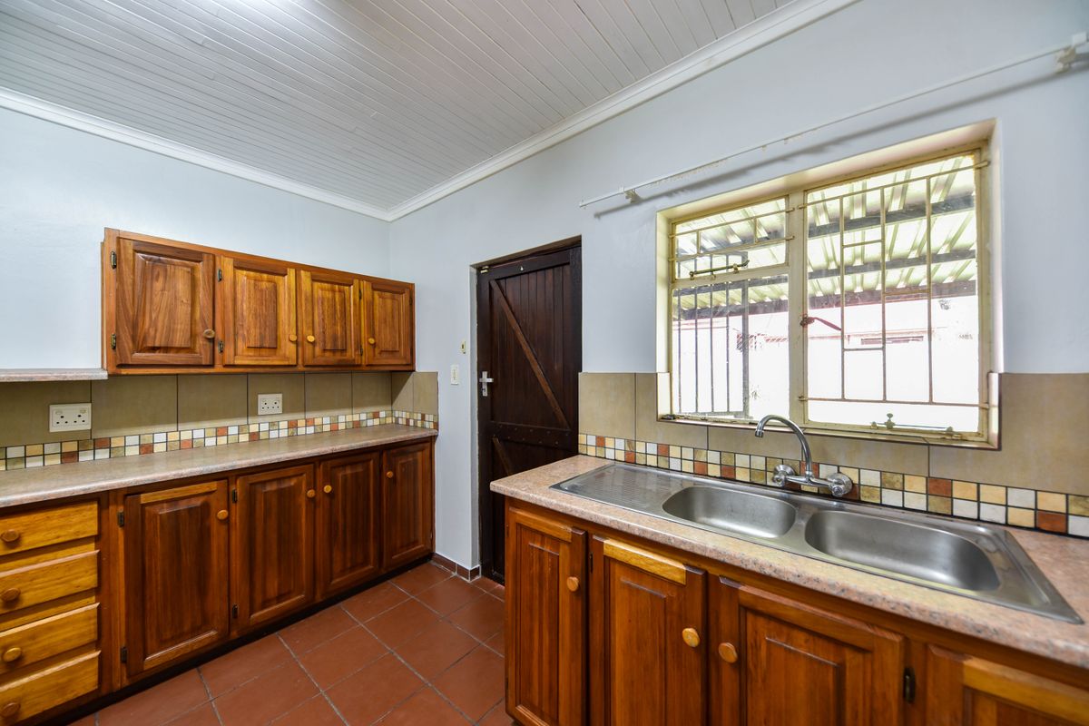 A functional kitchen featuring wooden cabinetry, double stainless steel sink, tiled splashback, and terracotta flooring with a timber ceiling.