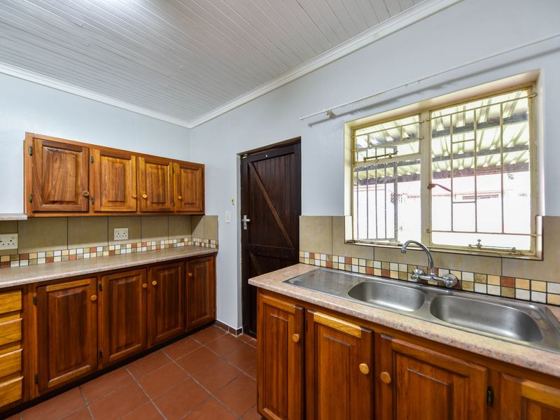 A functional kitchen featuring wooden cabinetry, double stainless steel sink, tiled splashback, and terracotta flooring with a timber ceiling.