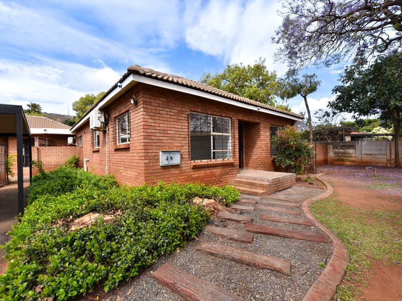A detached face brick house featuring a tiled roof, security bars on windows, an external air conditioning unit, and a paved garden walkway.