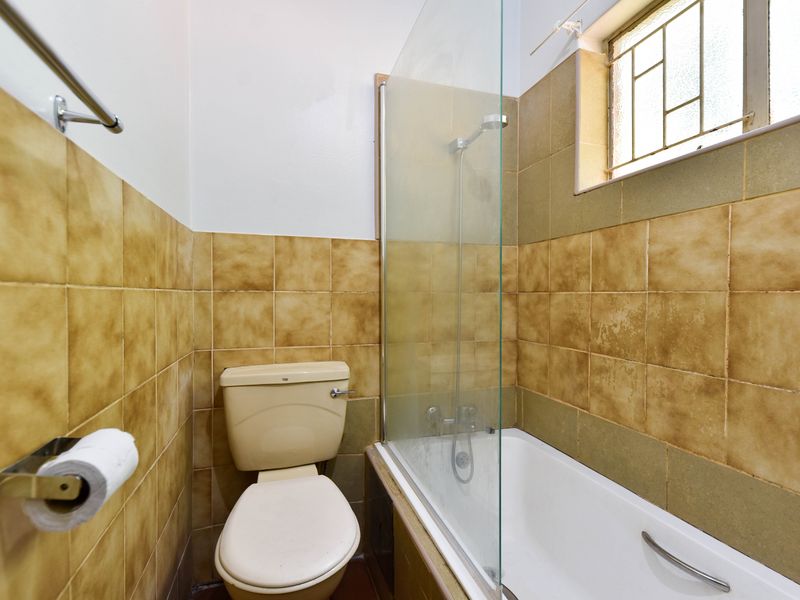 A compact bathroom featuring a bathtub with a glass shower screen, a toilet, and dated wall tiling.