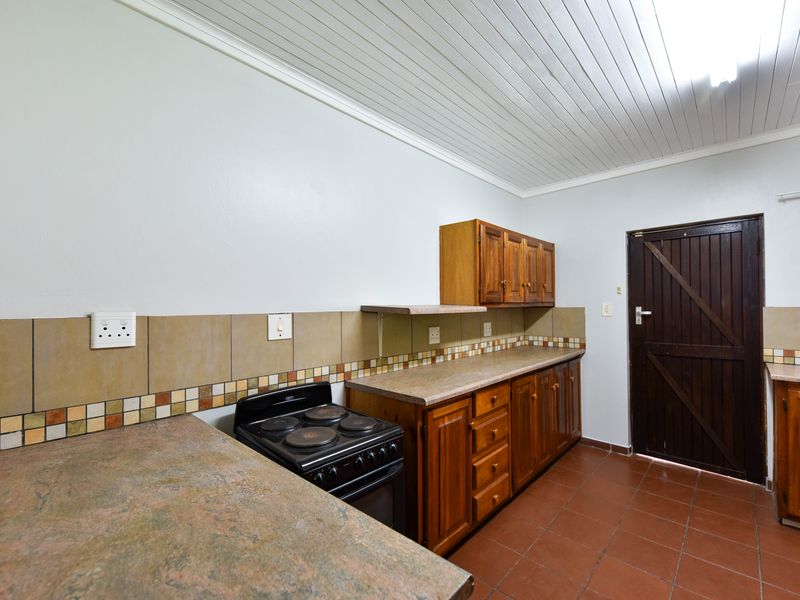 Functional kitchen featuring wooden cabinetry, laminate countertops, tiled backsplash, and a freestanding stove with direct access to an exterior door.