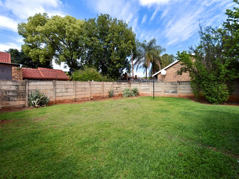 A spacious rear garden featuring a well-maintained lawn, enclosed by a precast concrete boundary wall with security razor wire.