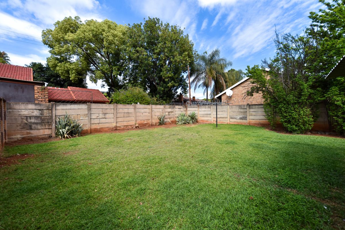 A spacious rear garden featuring a well-maintained lawn, enclosed by a precast concrete boundary wall with security razor wire.