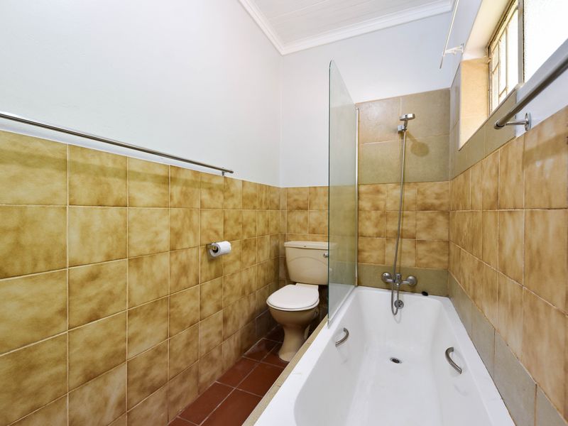 A functional bathroom featuring a bathtub with a glass shower screen, toilet, and neutral tiled finishes throughout.