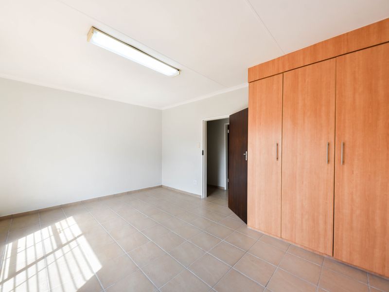 A clean, empty bedroom featuring neutral tiled flooring and ample built-in wooden cupboards, offering a versatile space ready for personalization.