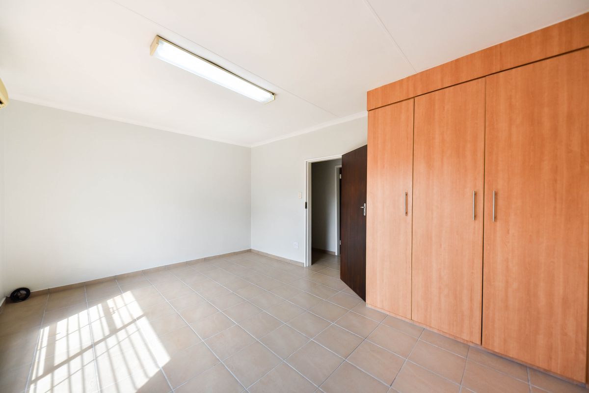 A clean, empty bedroom featuring neutral tiled flooring and ample built-in wooden cupboards, offering a versatile space ready for personalization.