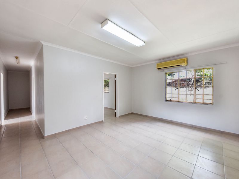 An empty, neutrally painted living area featuring tiled flooring, a wall-mounted air conditioning unit, and security bars on the windows.