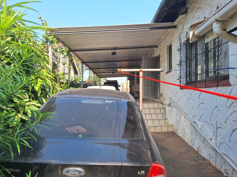 A covered side patio area featuring a metal carport structure, tiled steps leading to the entrance, and brick paving.