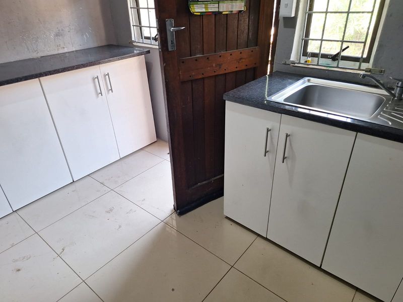 A functional kitchen area featuring white built-in cabinetry, dark laminate countertops, a stainless steel sink, and tiled flooring.