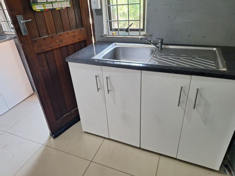 A functional scullery area featuring a stainless steel sink, laminate countertop, and white base cabinetry with modern handles.