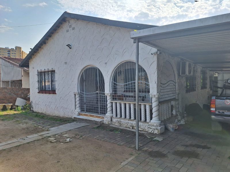Front elevation of a house featuring a carport, security gates, and textured facade, showing signs of wear and requiring exterior maintenance.