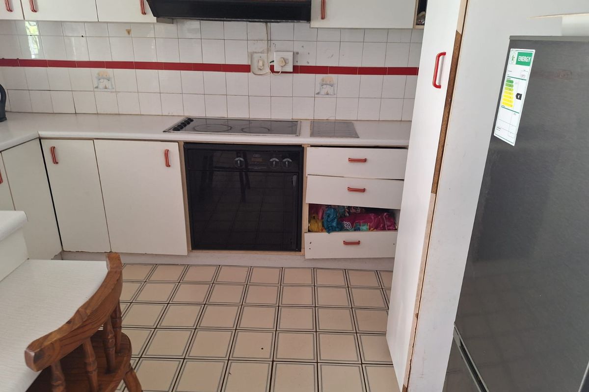A dated kitchen featuring white cabinetry, an integrated electric cooktop and oven, tiled backsplash, and tiled flooring, requiring cosmetic updates and repairs.