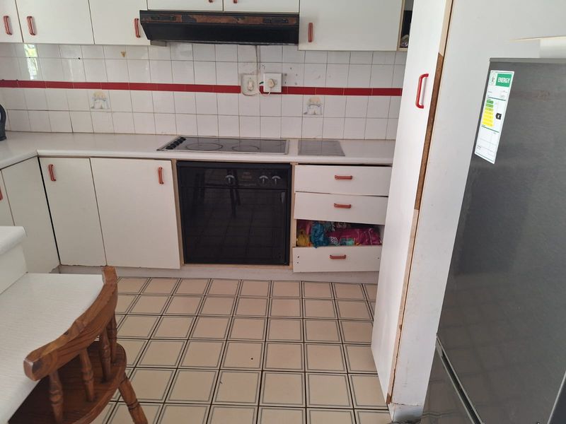 A dated kitchen featuring white cabinetry, an integrated electric cooktop and oven, tiled backsplash, and tiled flooring, requiring cosmetic updates and repairs.