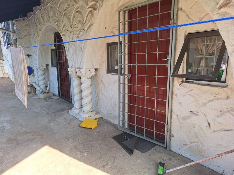 A covered patio area featuring decorative architectural columns, security gates, and textured wall finishes, offering potential for outdoor living space enhancement.
