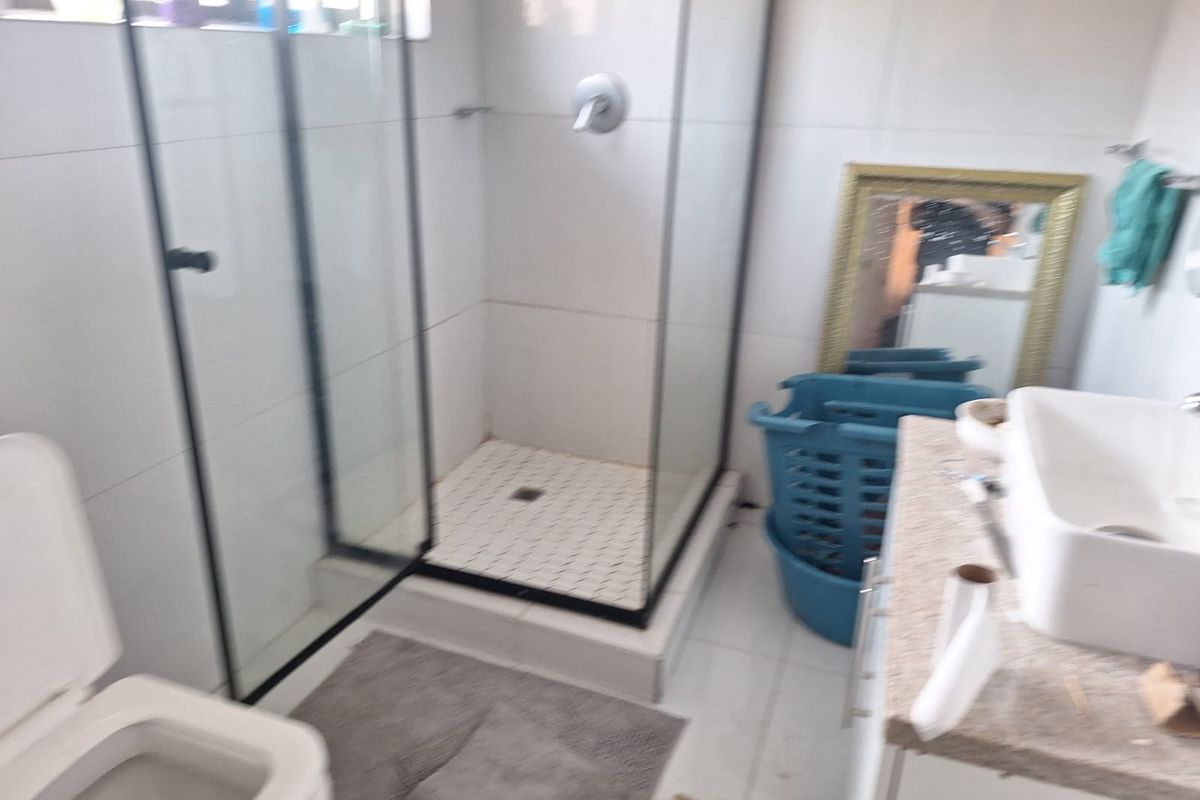 A functional bathroom featuring a glass-enclosed shower, a vanity basin, and a toilet with neutral wall and floor tiling.