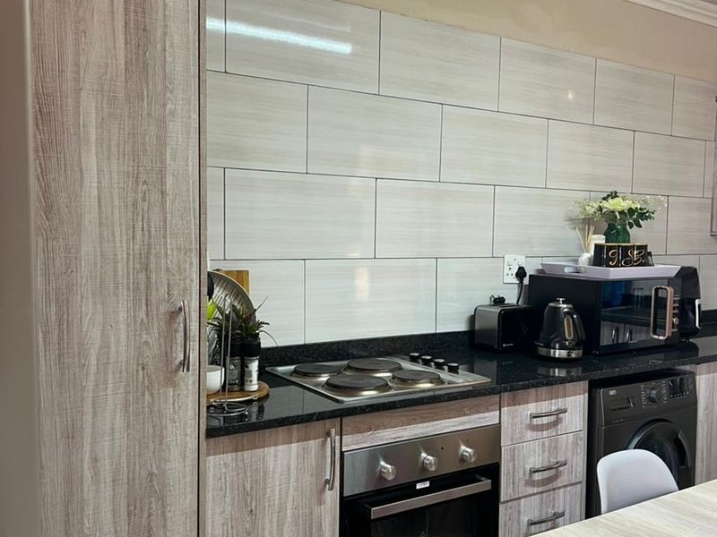 Modern kitchen featuring wood-look cabinetry, granite countertops, subway tile backsplash, and built-in oven with electric hob.