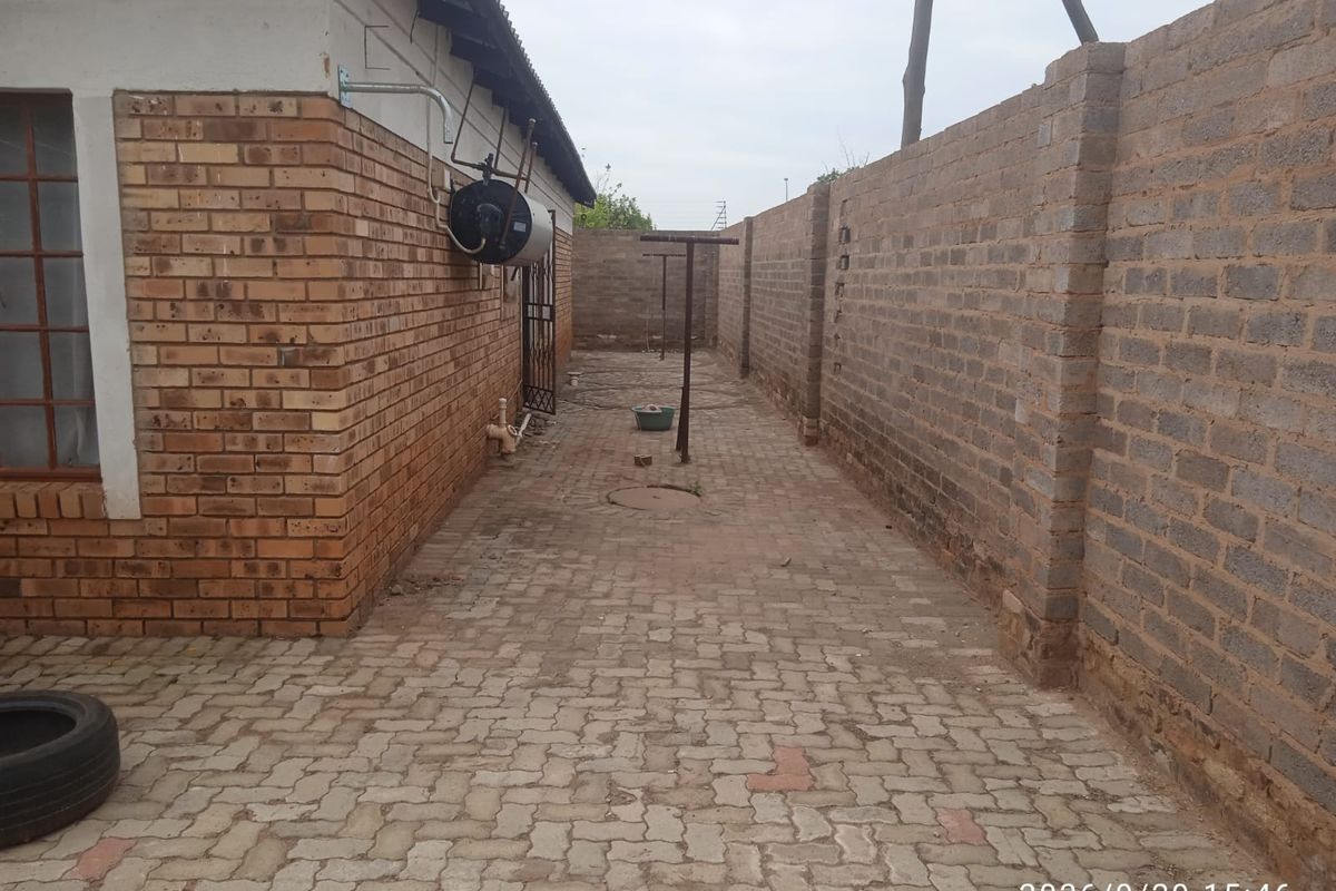 A narrow rear exterior area featuring brick paving, a boundary wall, and an external geyser unit.