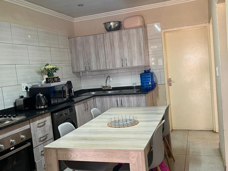 A functional kitchen featuring wood-look cabinetry, laminate countertops, integrated oven and hob, and tiled flooring with a central dining area.