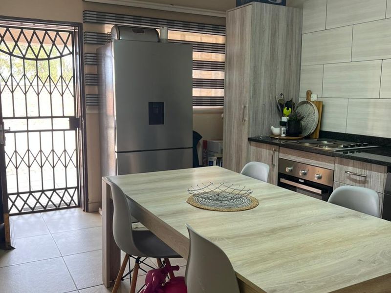 A functional kitchen area featuring built-in cabinetry, an integrated oven and hob, tiled flooring, and direct access to the exterior via a security gate.