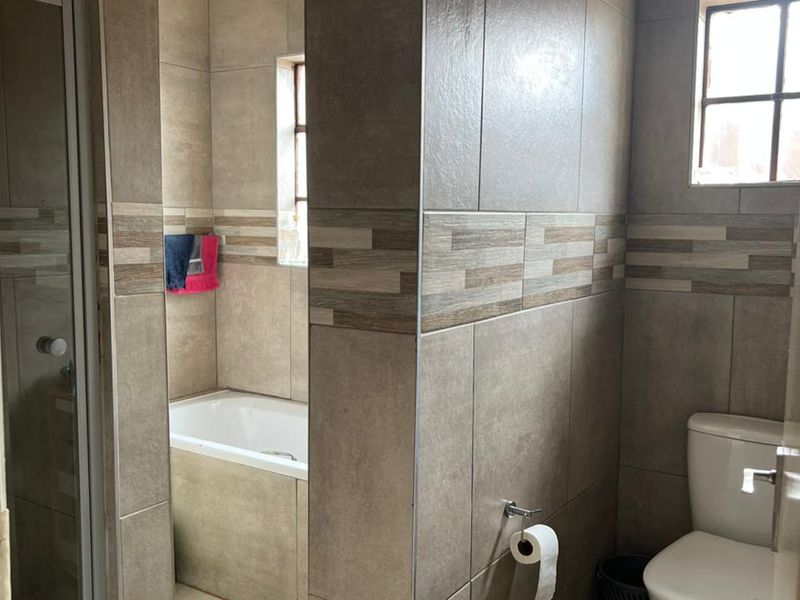 A functional bathroom featuring a built-in bathtub, separate shower enclosure, and toilet, finished with neutral-toned wall and floor tiles.