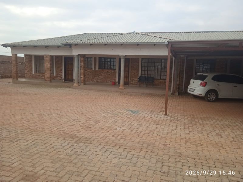 A single-story face brick house featuring a covered patio, metal roof, and an attached carport with a paved driveway.