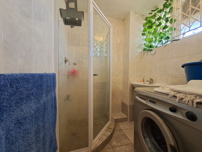 Compact bathroom featuring a shower enclosure, basin, and tiled finishes. The space includes integrated laundry plumbing connections.