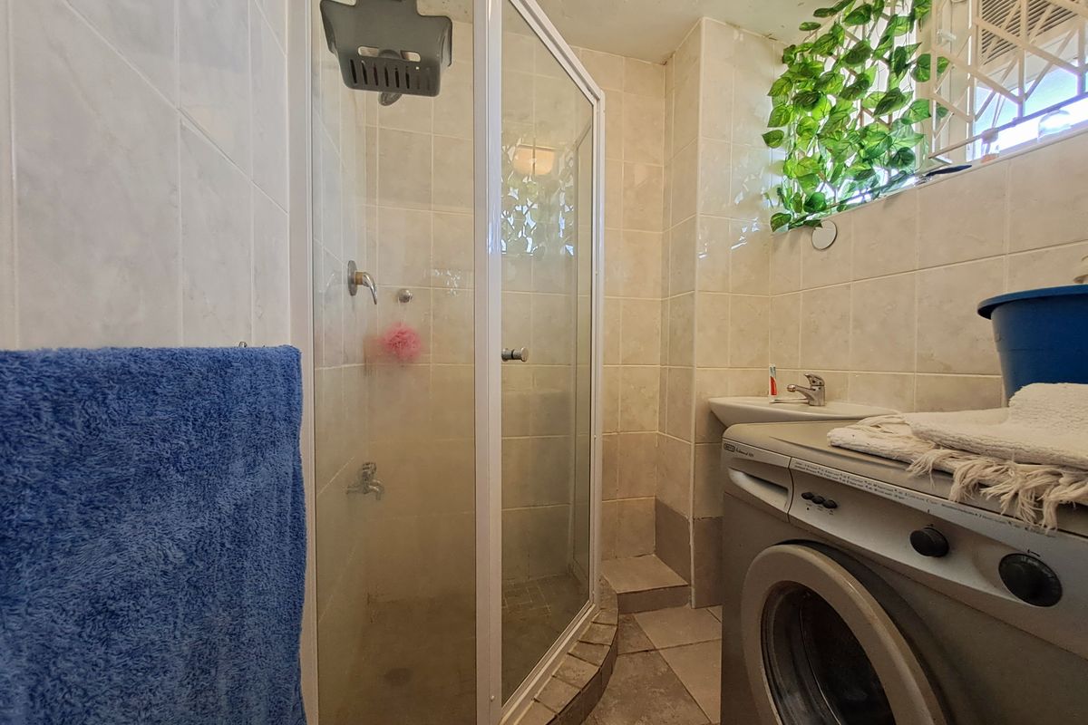 Compact bathroom featuring a shower enclosure, basin, and tiled finishes. The space includes integrated laundry plumbing connections.