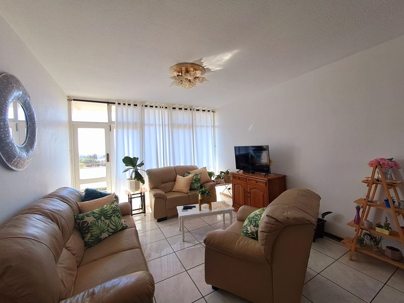 A bright living room featuring tiled flooring and a glass sliding door leading to an outdoor area, providing natural light throughout the space.