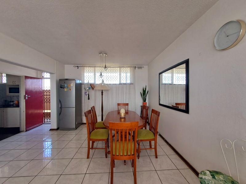 Open-plan dining area featuring ceramic floor tiles, security bars on windows, and direct access to the kitchen and exterior entrance.
