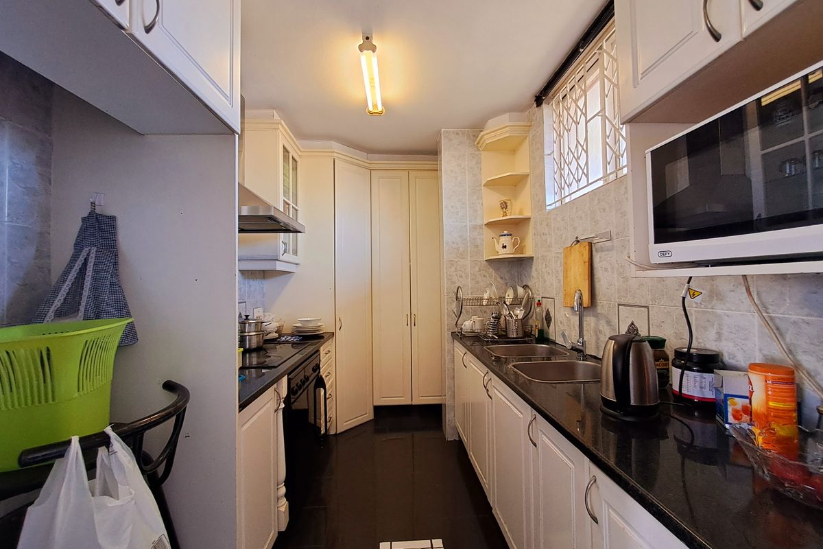 A functional galley-style kitchen featuring white cabinetry, dark countertops, a double basin sink, and built-in appliances including a hob and microwave.