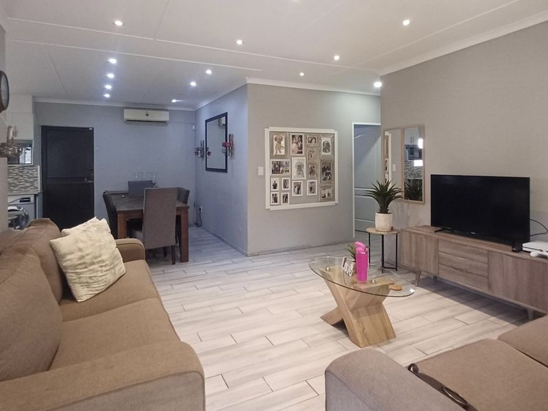Spacious open-plan living and dining area featuring modern tiled flooring, recessed downlighting, and a wall-mounted air conditioning unit.