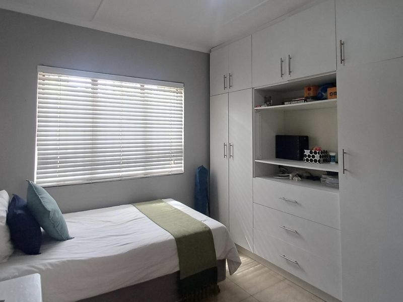 A well-maintained bedroom featuring ample built-in storage cupboards, tiled flooring, and venetian blinds for privacy.