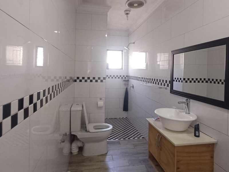 A functional bathroom featuring tiled walls with a decorative border, a vessel sink on a wooden vanity, and a walk-in shower area.