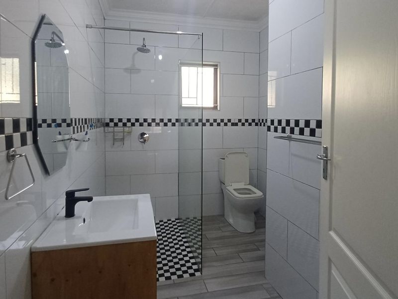A modern, clean bathroom featuring a vanity with basin, a glass-enclosed shower, and a toilet, finished with contemporary black and white tiled accents.