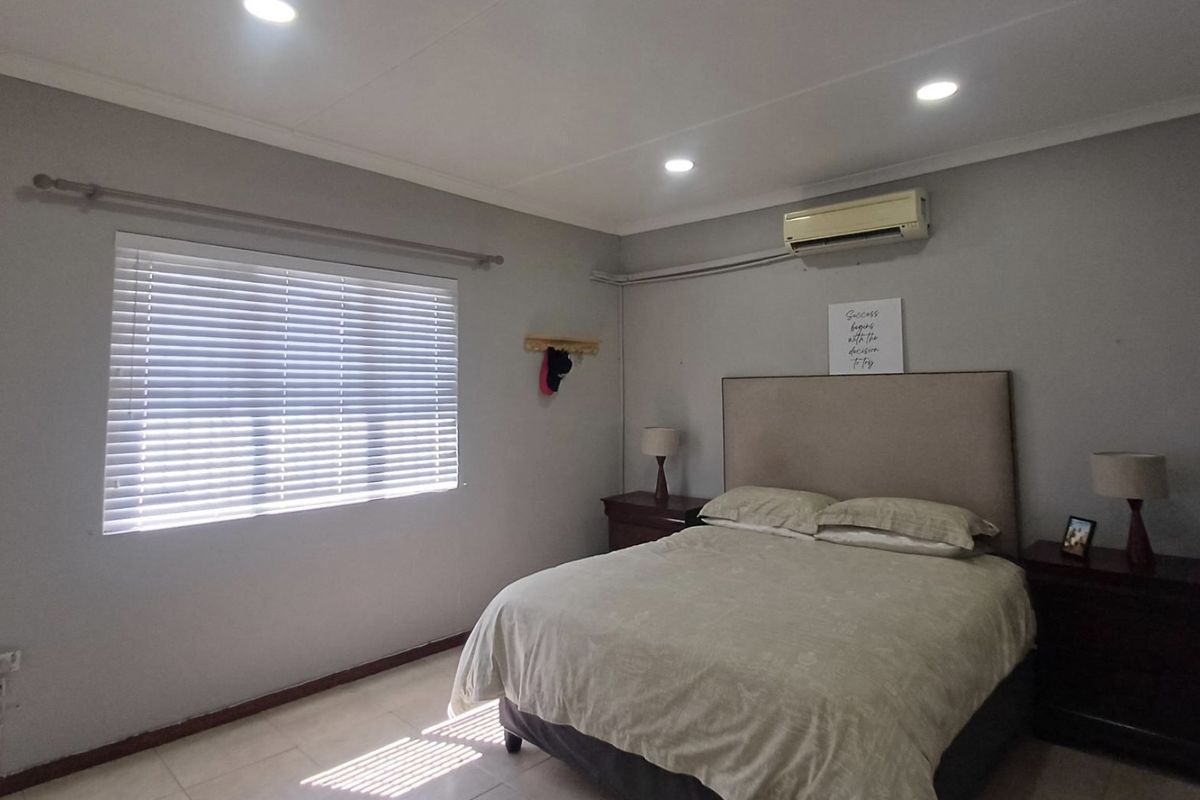 A well-maintained bedroom featuring tiled flooring, recessed downlighting, and a wall-mounted split-system air conditioning unit.