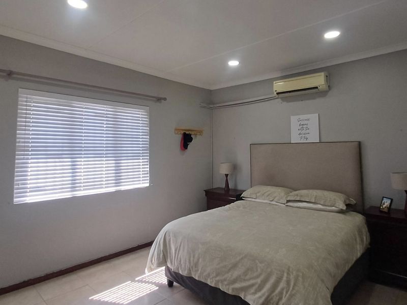 A well-maintained bedroom featuring tiled flooring, recessed downlighting, and a wall-mounted split-system air conditioning unit.