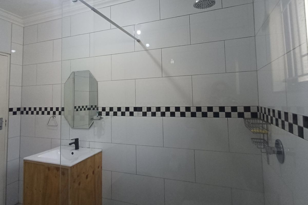 A clean bathroom featuring white wall tiles with a decorative checkered border, a wooden vanity cabinet, and a glass-enclosed shower area.