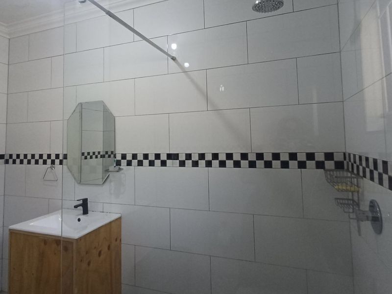 A clean bathroom featuring white wall tiles with a decorative checkered border, a wooden vanity cabinet, and a glass-enclosed shower area.